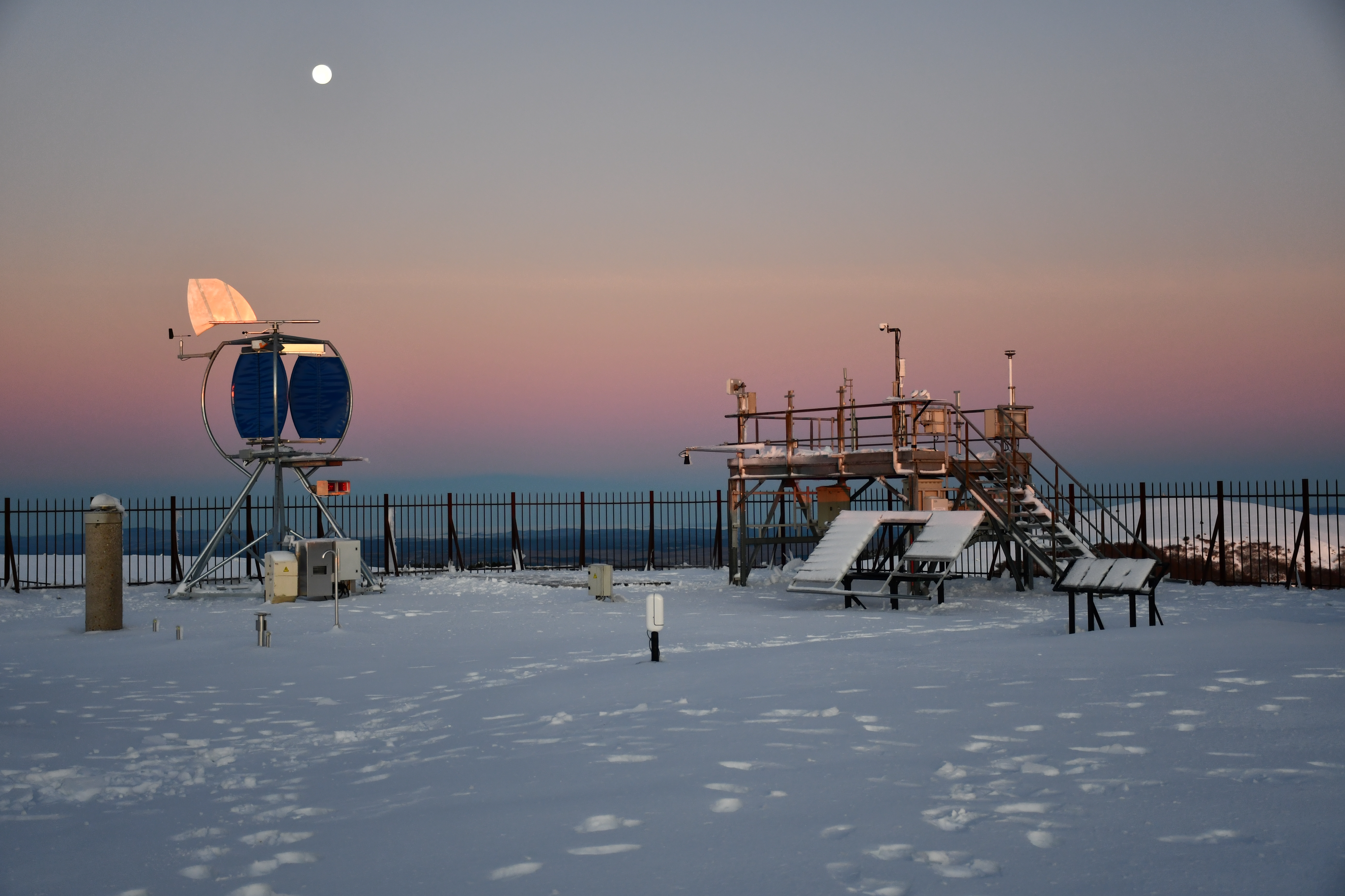 Plateforme d'essais enneigée au crépuscule, pleine lune, éolienne à axe vertical givrée